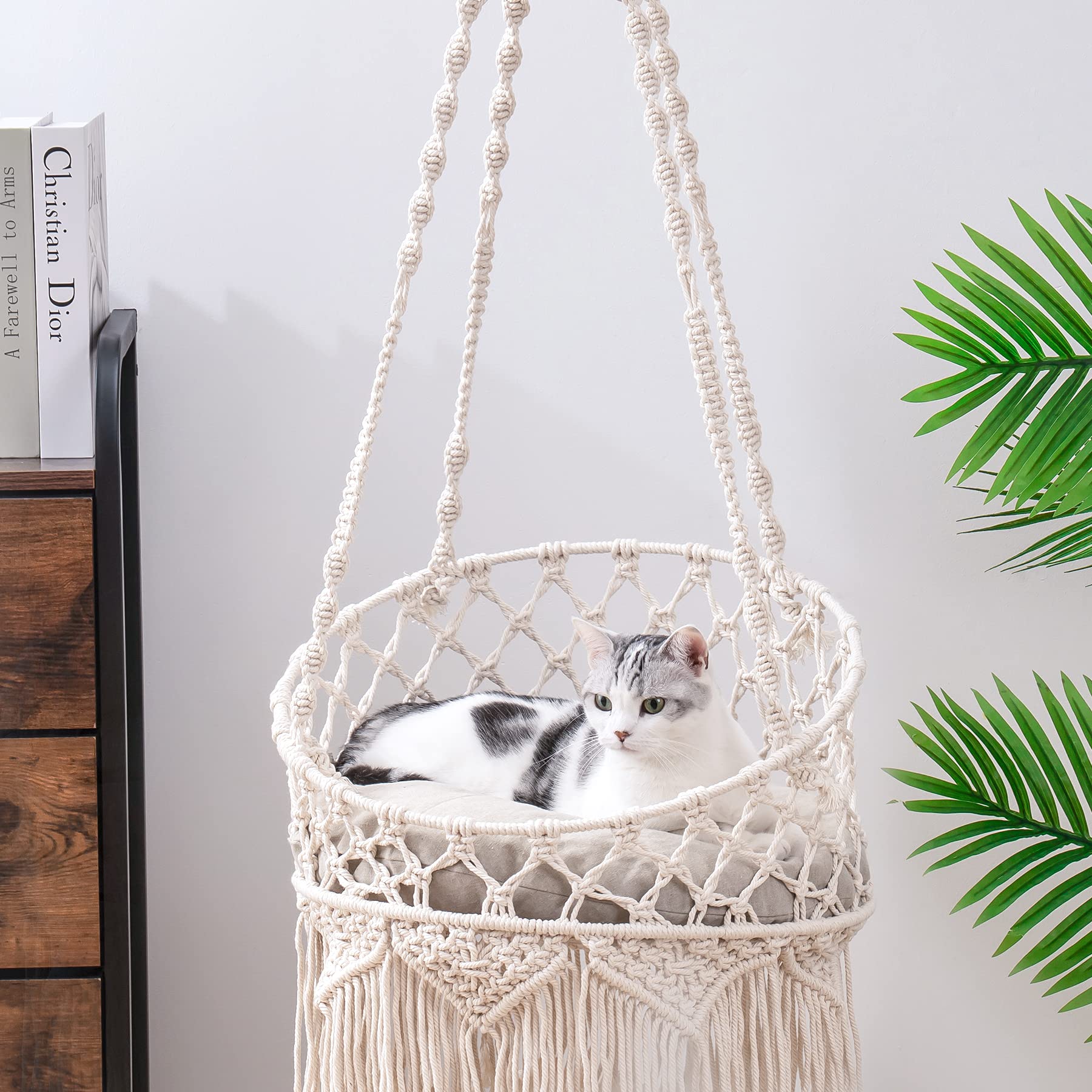 A white and grey cat relaxing in a handwoven macramé cat hammock 